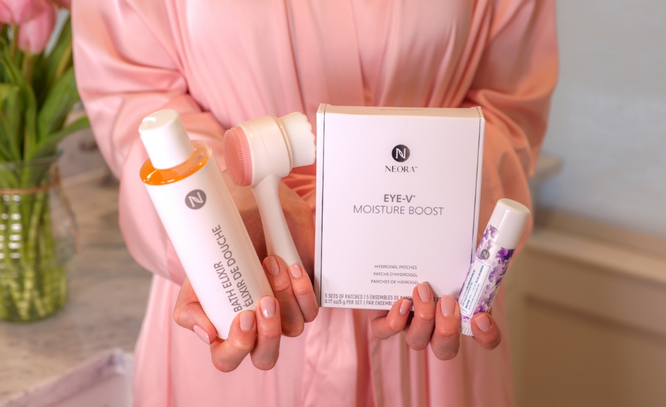 Woman holding Neora’s Make Her Mother’s Day Bundle which includes: Zen + Calm Lavender Balm, Bath Elixir, Eye-V Moisture Boost Hydrogel Patches and a FREE dual-sided Facial Scrubber